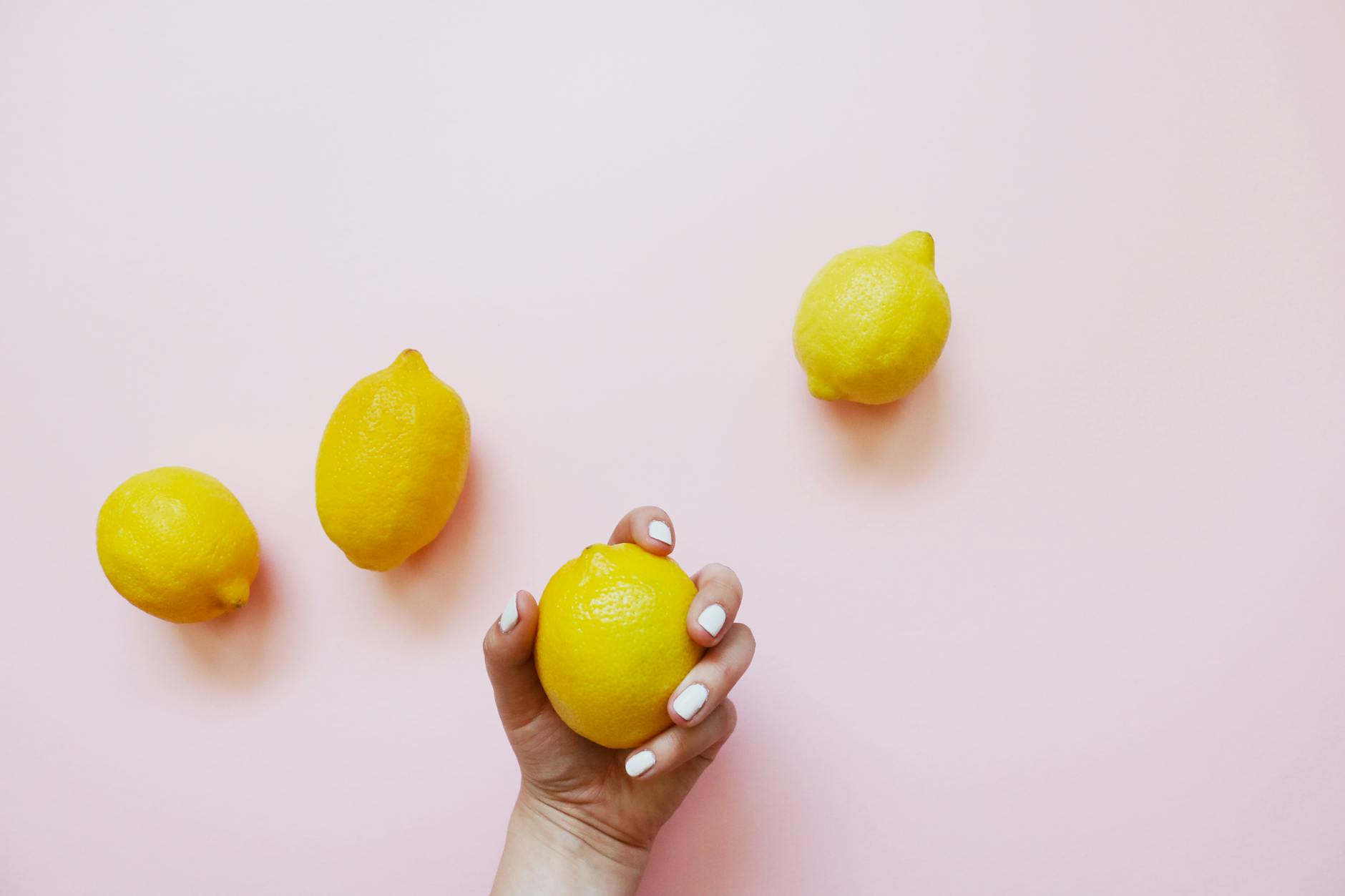 Hand holding a fresh lemon on a soft pink background, symbolizing renewal and vitality