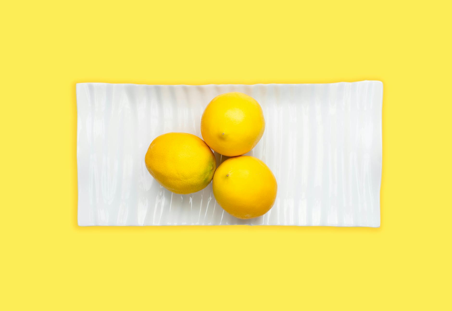 Fresh lemons on a white plate with a vibrant yellow background, representing the lemon vibrator experience